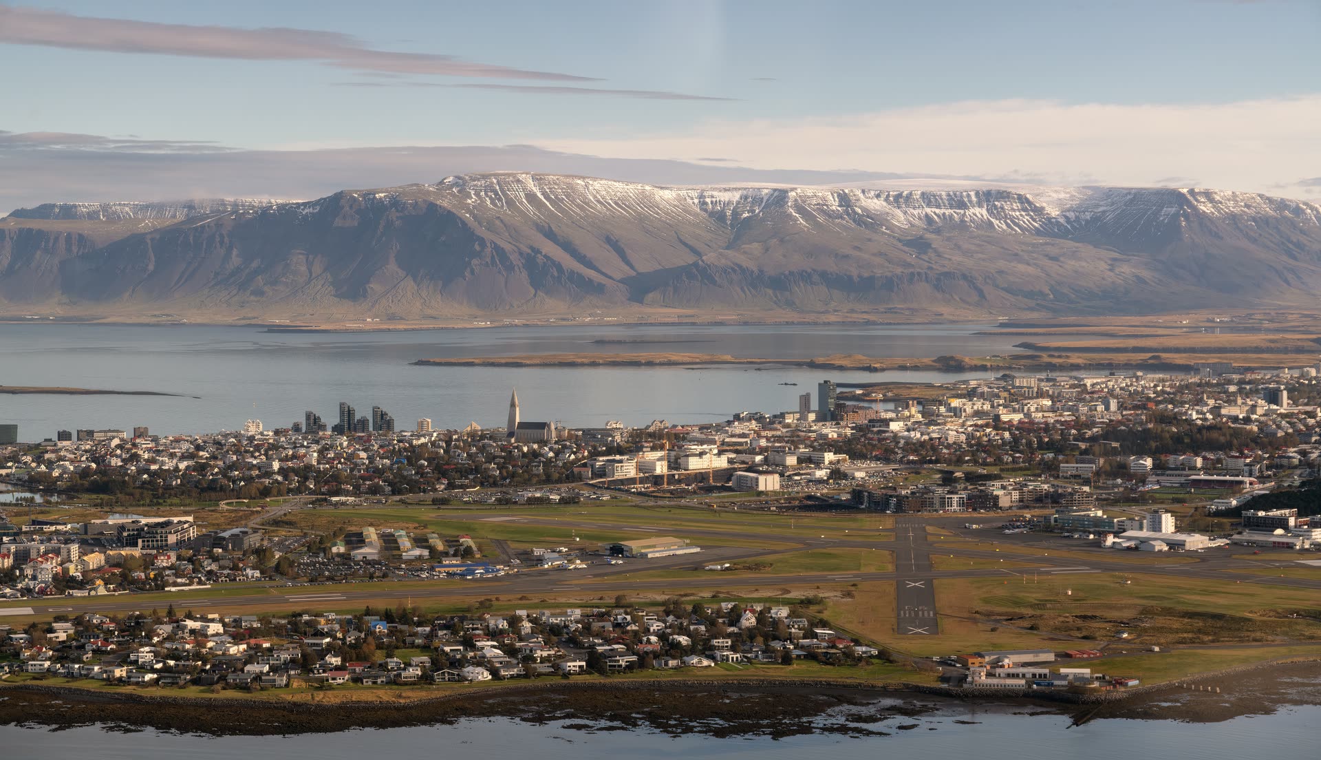 Reykjavík úr lofti: Skerjafjörður og Reykjavíkurflugvöllur í forgrunni, miðborgin og Hallgrímskirkja handan við og Esja í baksýn.